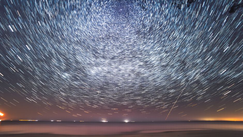 Cautivadoras estelas de estrellas crean patrones hipnóticos sobre un sereno paisaje marino nocturno.