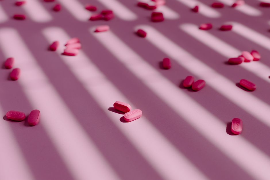 Píldoras rosas dispersas sobre una superficie con sombras a rayas. Composición minimalista y artística.