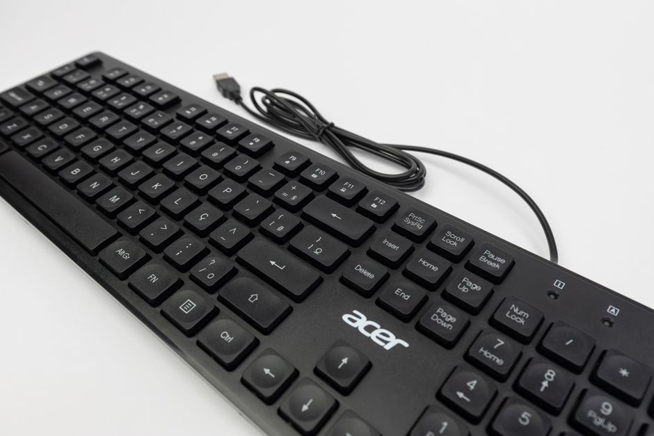 Primer plano de un teclado negro con cable en un fondo blanco, enfatizando la tecnología.
