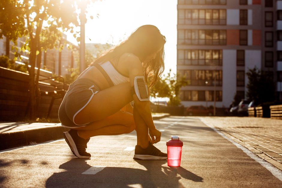 Una mujer preparándose para hacer ejercicio al aire libre durante la hora dorada, atándose los zapatos en una calle de la ciudad.