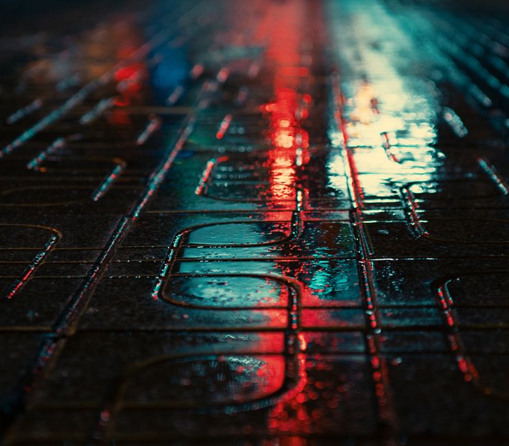 Escena callejera urbana melancólica con reflejos coloridos sobre el pavimento mojado por la noche.