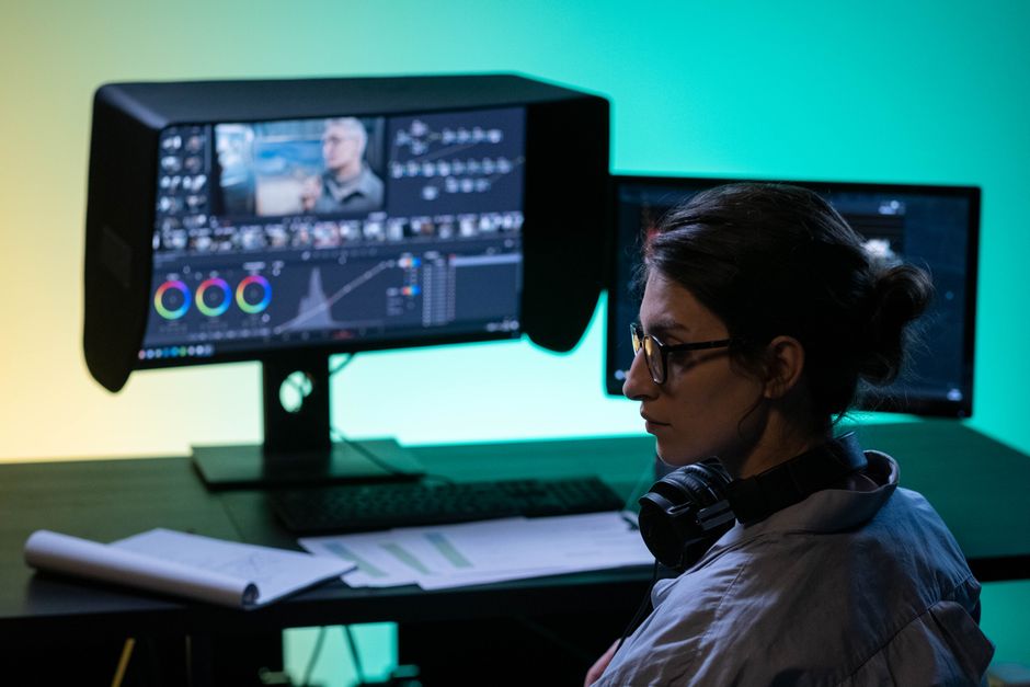 Editora de vídeo enfocada trabajando en un setup de pantallas duales con iluminación ambiental colorida.