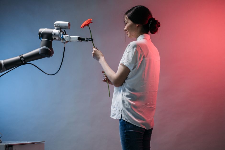Una mujer interactúa con un brazo robótico que sostiene una flor, mostrando tecnología y conexión humana.