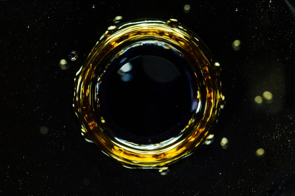 Un primer plano creativo de la dinámica del líquido con un centro oscuro rodeado de reflejos dorados y pequeñas burbujas.