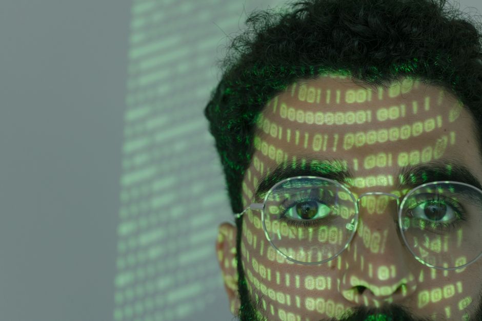 Primer plano de un hombre con código binario proyectado en su cara, simbolizando la ciberseguridad.