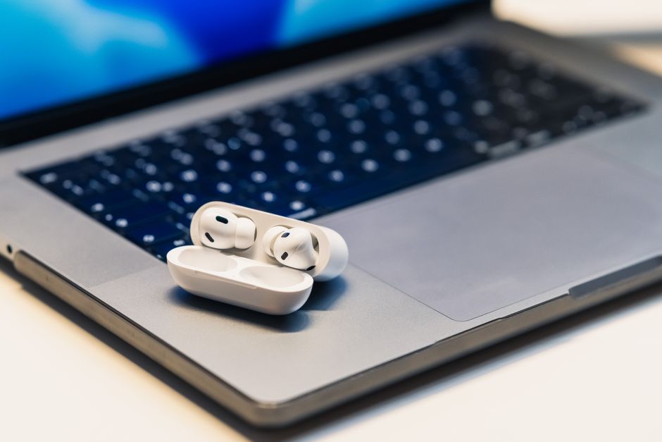 Primer plano de unos auriculares inalámbricos en un estuche colocado sobre una computadora portátil abierta, resaltando la tecnología moderna.