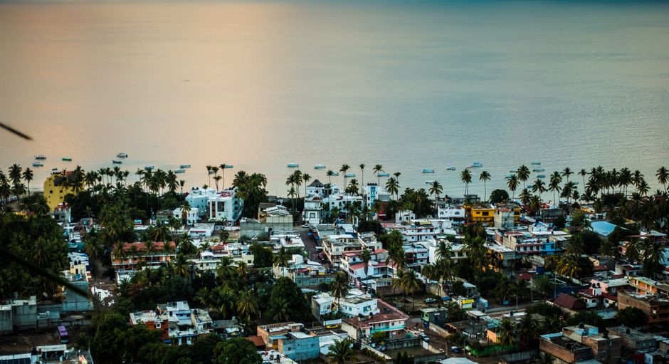 Vista aérea de un pueblo costero mexicano con palmeras y océano durante el día.