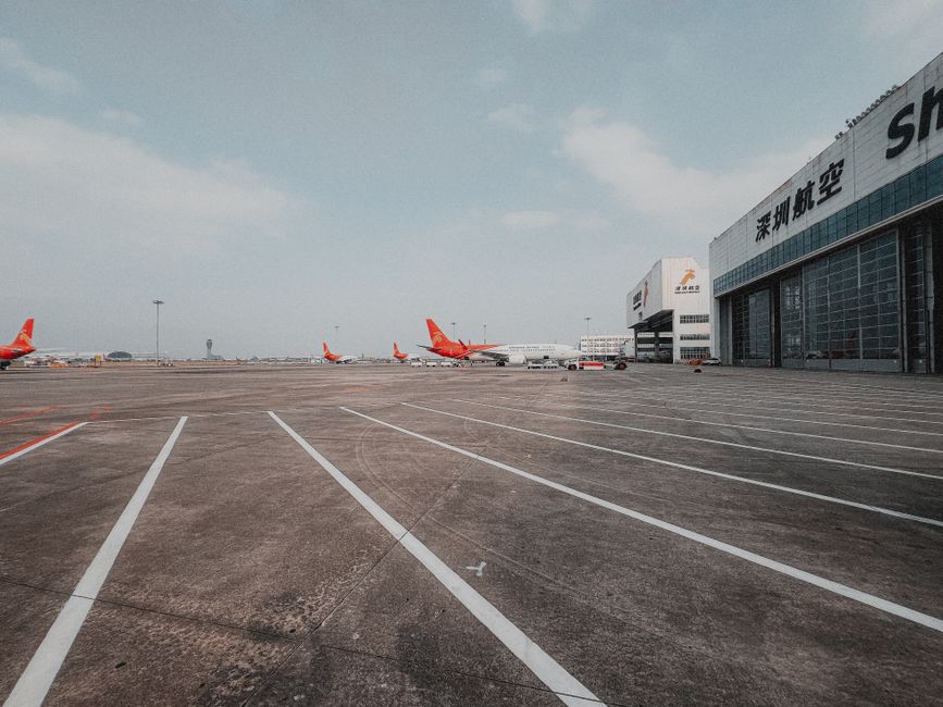 Una pista de aeropuerto amplia con aviones y hangares bajo un cielo despejado.