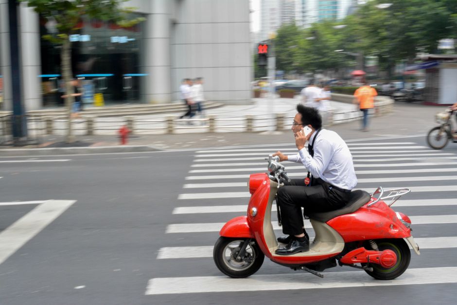 Empresario conduciendo un scooter rojo mientras habla por teléfono en Shanghái, China.