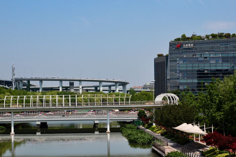Un paisaje urbano moderno con una autopista elevada, un canal y un edificio comercial bajo un cielo despejado.