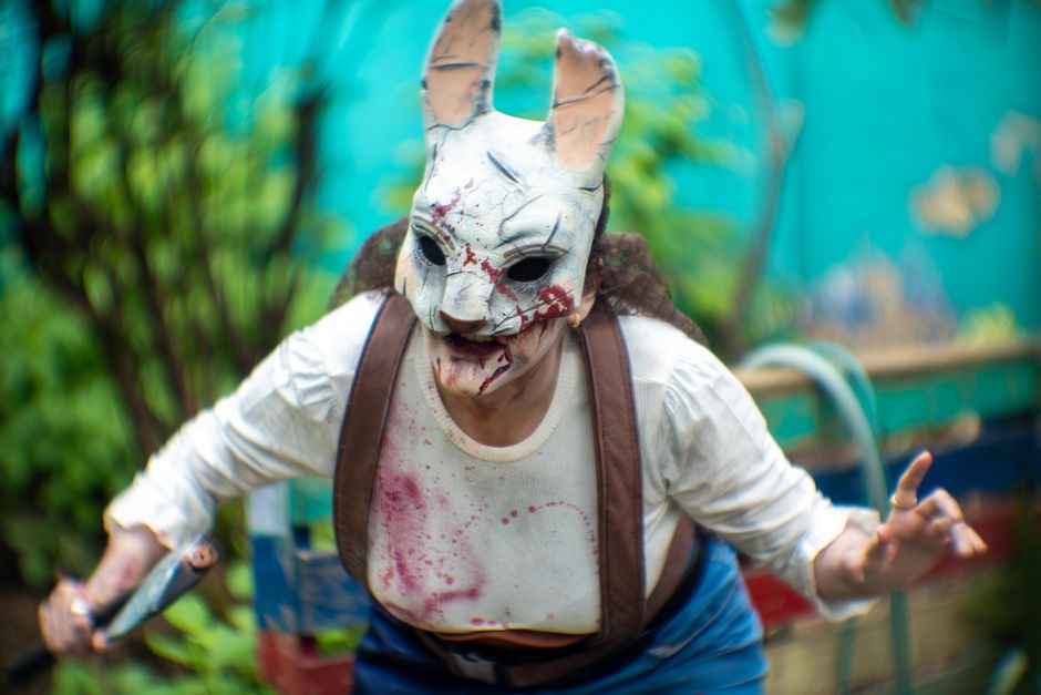 Una persona con una aterradora máscara de conejo hace cosplay de horror al aire libre entre una vegetación vibrante.