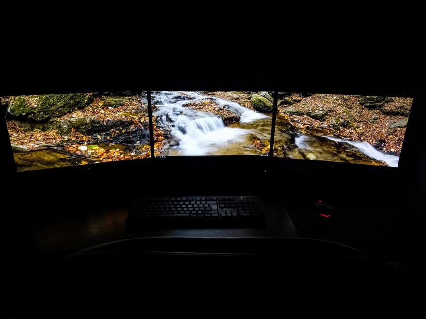 Espacio de trabajo oscuro con una configuración de tres monitores que muestra una escena serena de cascada.