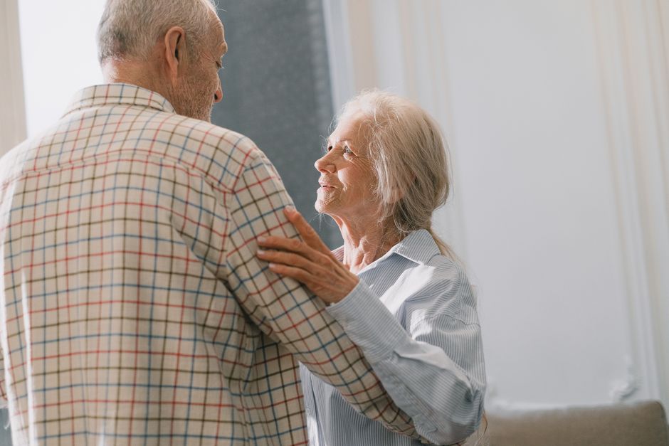 Pareja de ancianos compartiendo un baile tierno en interiores, destacando el amor y la compañía en los años dorados.