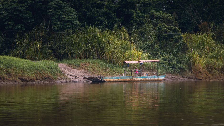 Un barco rústico está atracado en una exuberante orilla del río en Moyobamba, Perú, rodeado de densa vegetación.