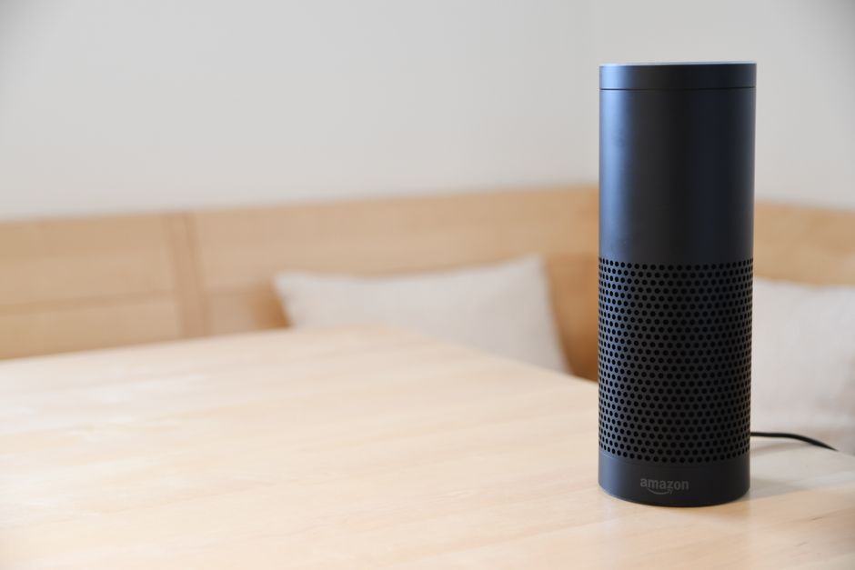 Un altavoz inteligente negro descansando sobre una mesa de madera de color claro en un acogedor ambiente interior.