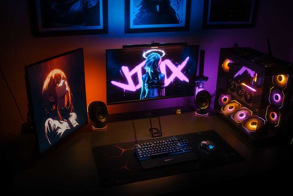 Una configuración de juego moderna con iluminación RGB, monitores duales y una PC personalizada con componentes coloridos.
