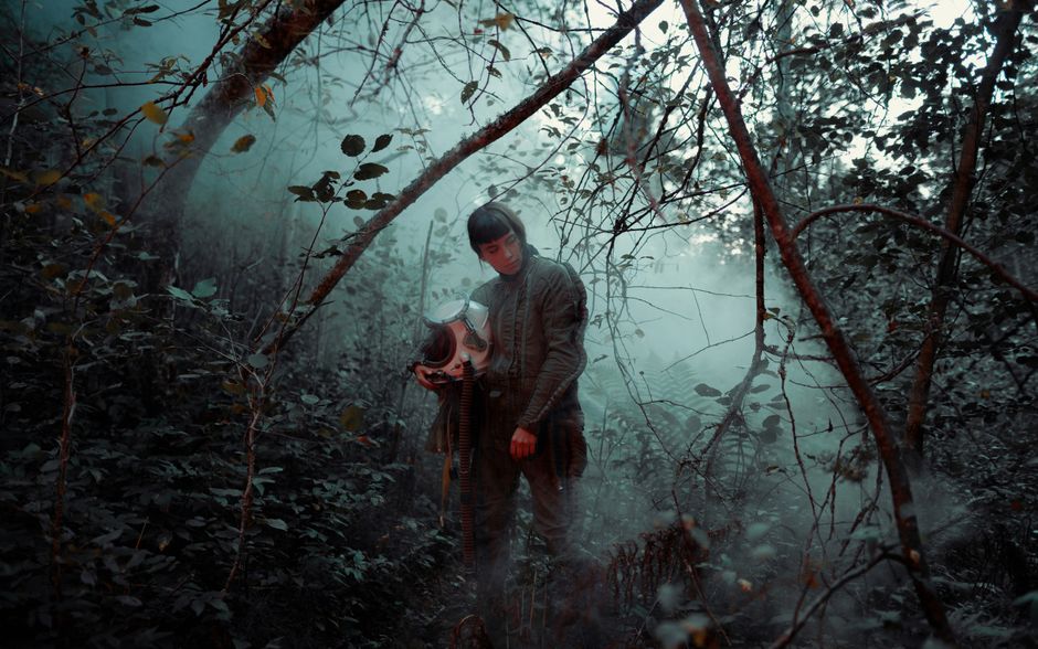 Un hombre en un bosque nebuloso sosteniendo un casco, creando un ambiente misterioso.