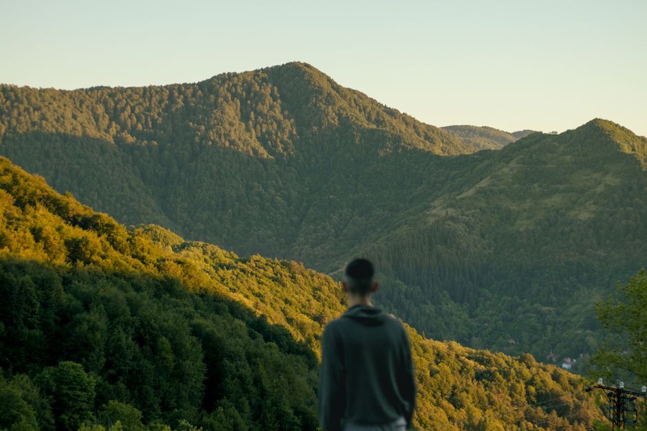 Un hombre solitario se encuentra mirando un impresionante paisaje montañés verde bajo cielos despejados.