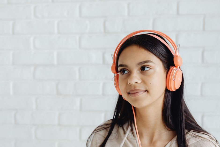 Retrato de una joven con auriculares naranjas frente a un fondo de ladrillos blancos.