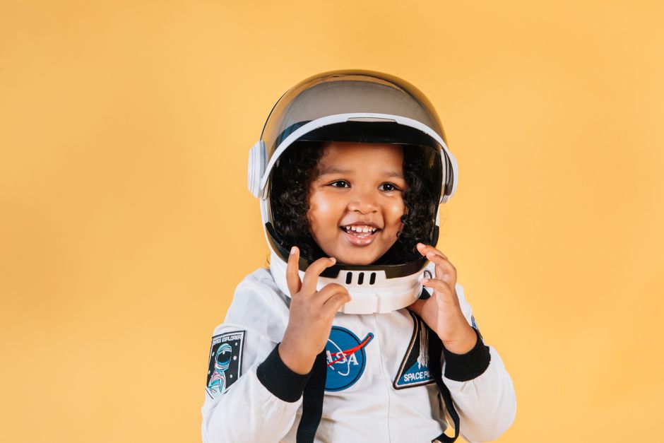 Adorable niña con disfraz de astronauta sonriendo contra un fondo amarillo.