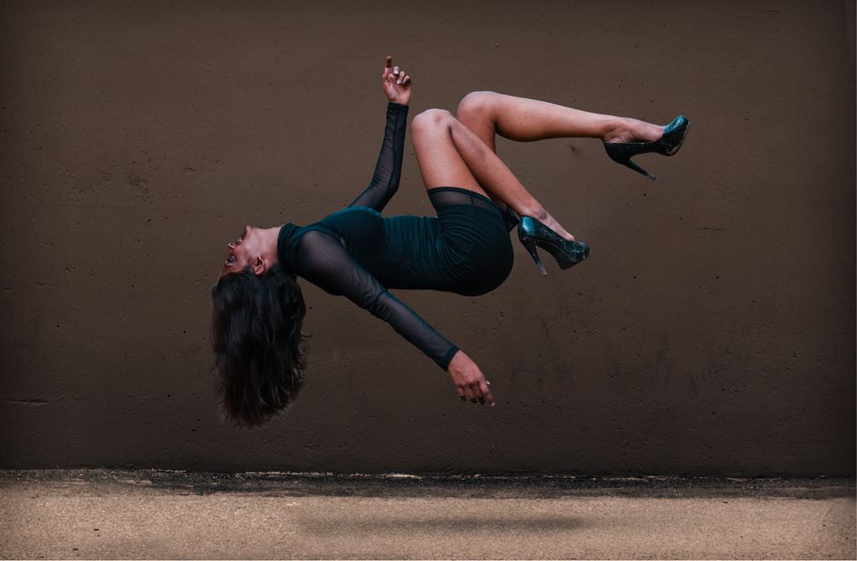 Una mujer en pose de levitación frente a una pared texturizada, vistiendo un vestido elegante.