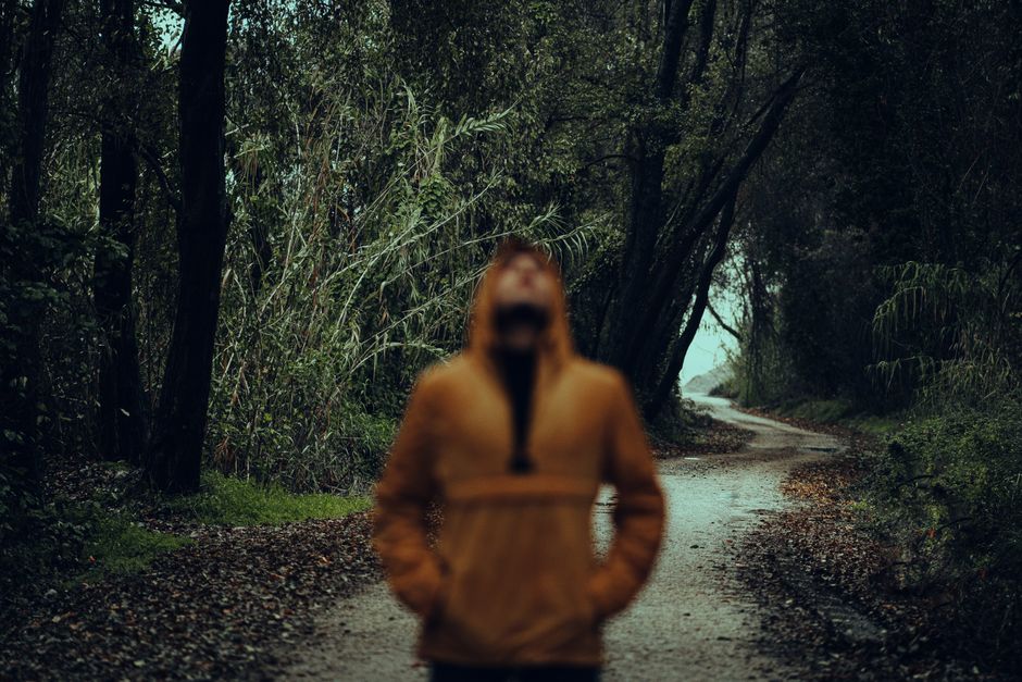 Persona borrosa con chaqueta amarilla de pie en un camino de tierra apartado en el bosque durante el día.