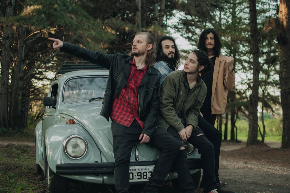 Cuatro hombres posando con un Volkswagen Escarabajo vintage en un parque, evocando una vibra clásica.