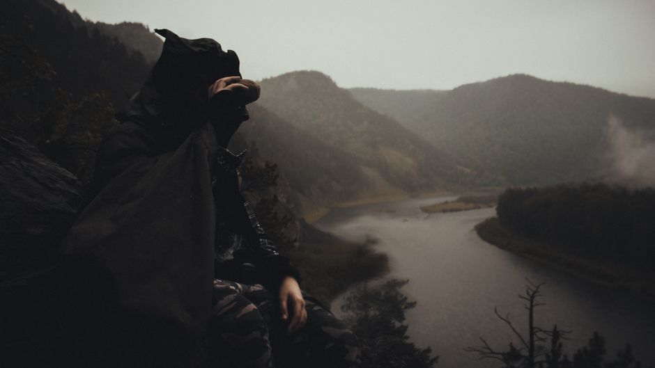 Un hombre con un impermeable se sienta en un lado de la montaña con vista a un río escénico.