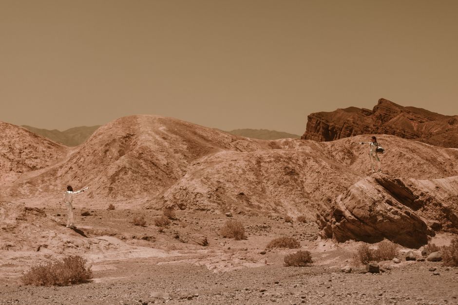 Dos astronautas en un paisaje desértico rocoso, evocando la exploración de Marte.