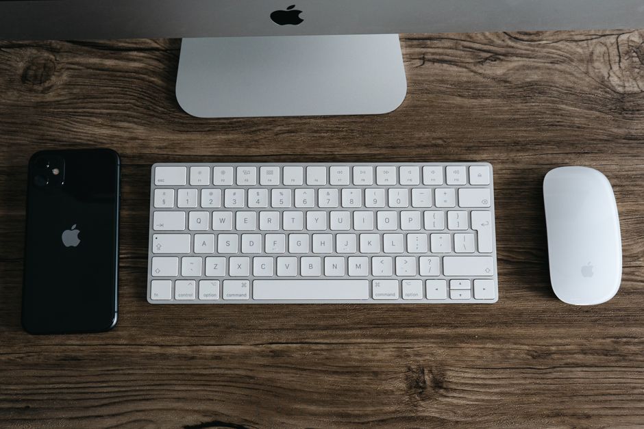 Un espacio de trabajo minimalista con un teléfono inteligente, teclado y ratón sobre un escritorio de madera.