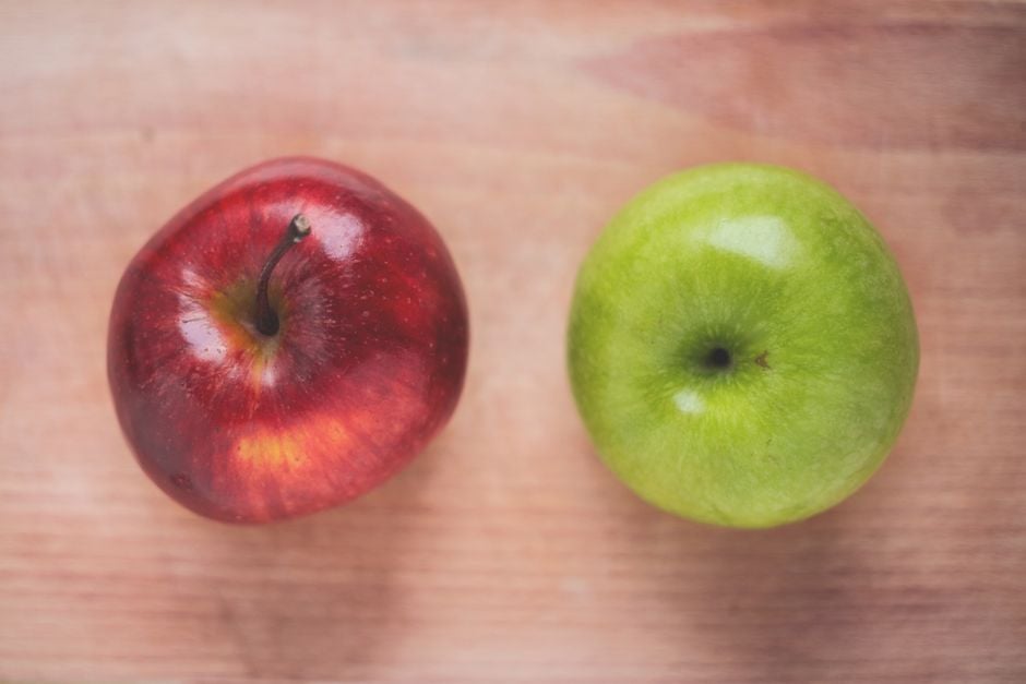 Primer plano de una manzana roja y una verde en una mesa de madera, ideal para temas de alimentación saludable.