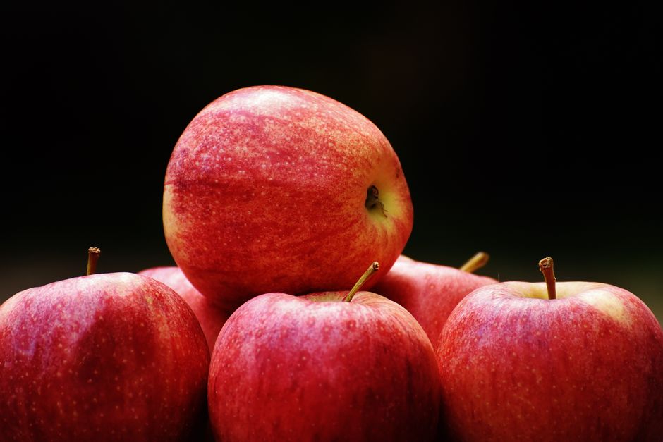 Un grupo de manzanas rojas maduras apiladas sobre un fondo oscuro que resalta su frescura y vitalidad.