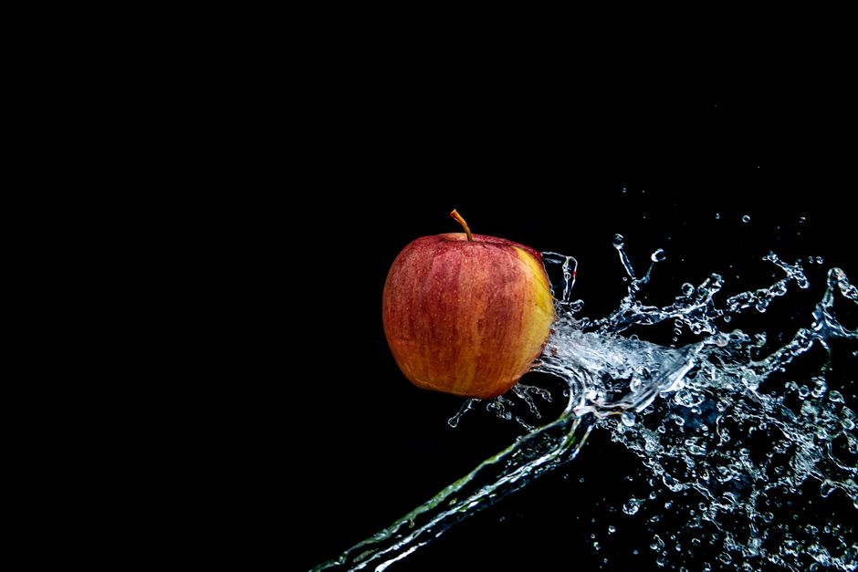 Vibrante manzana roja capturada con una dinámica salpicadura de agua contra un fondo oscuro.