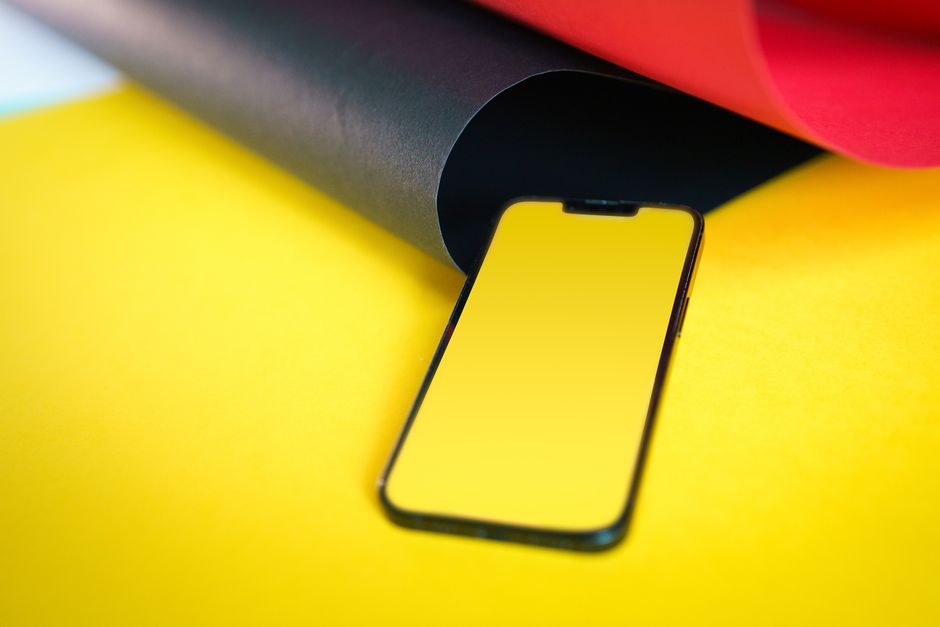 Smartphone con pantalla en blanco sobre fondo de papel rojo, negro y amarillo.