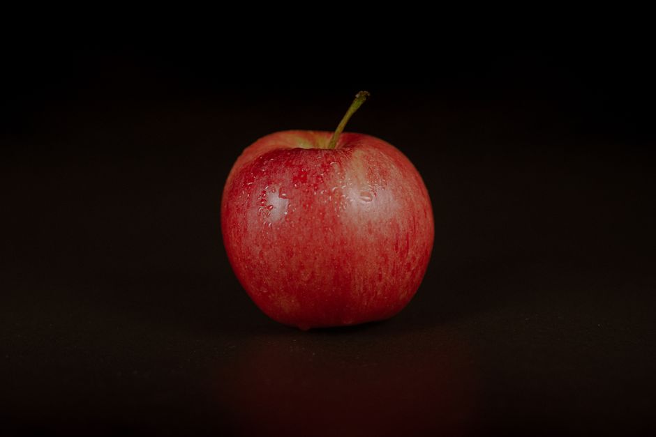 Acercamiento de una manzana roja fresca con gotas de agua sobre un fondo negro, mostrando la frescura de la fruta.