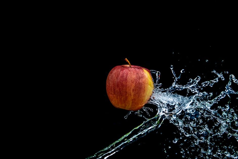 Vibrante manzana roja capturada con una dinámica salpicadura de agua contra un fondo oscuro.