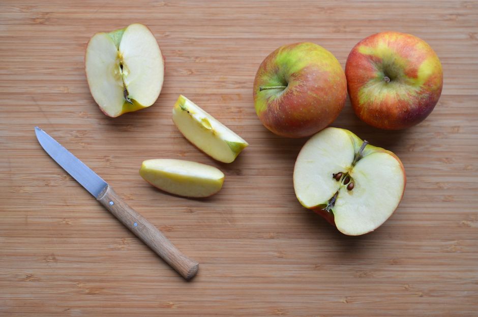 Manzanas coloridas en rodajas sobre una tabla de cortar de madera con un cuchillo, ideal para conceptos de comida saludable.