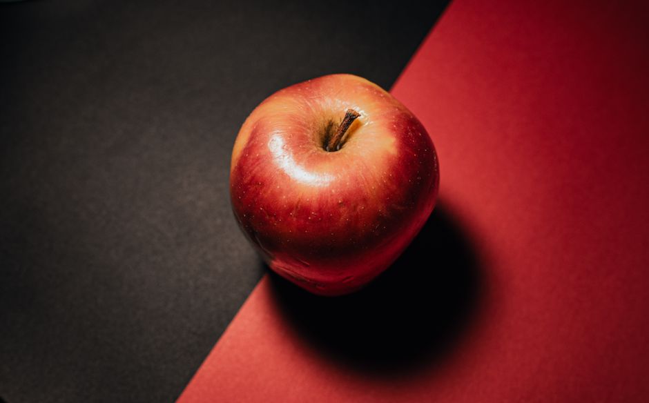 Una manzana roja madura brilla sobre un fondo negro y rojo contrastante, mostrando elegancia y simplicidad.
