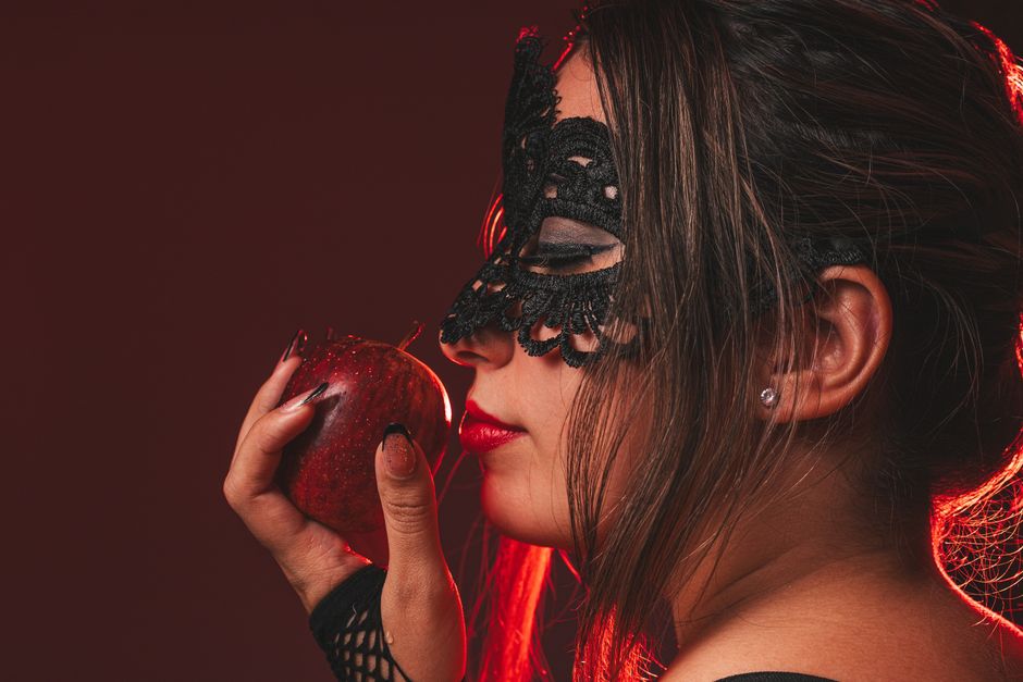 Mujer elegante con máscara de encaje sosteniendo una manzana. Retrato oscuro y melancólico con un toque de misterio.