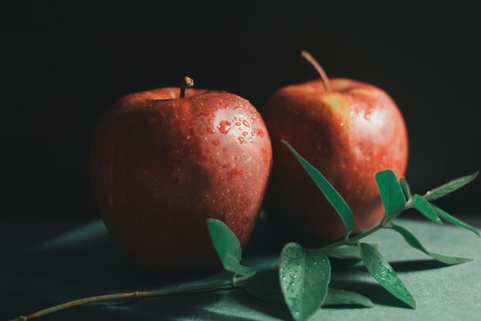 Manzanas rojas vibrantes con gotas de agua en una rama frondosa, ideales para conceptos de alimentos orgánicos.