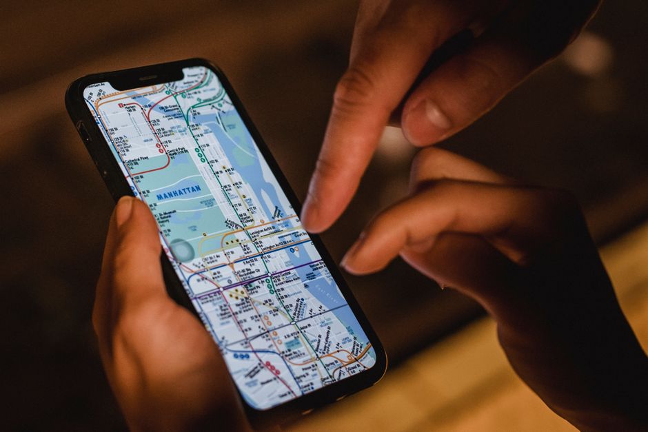 Primer plano de manos usando un smartphone con un mapa del metro de Nueva York por la noche, destacando la navegación moderna.