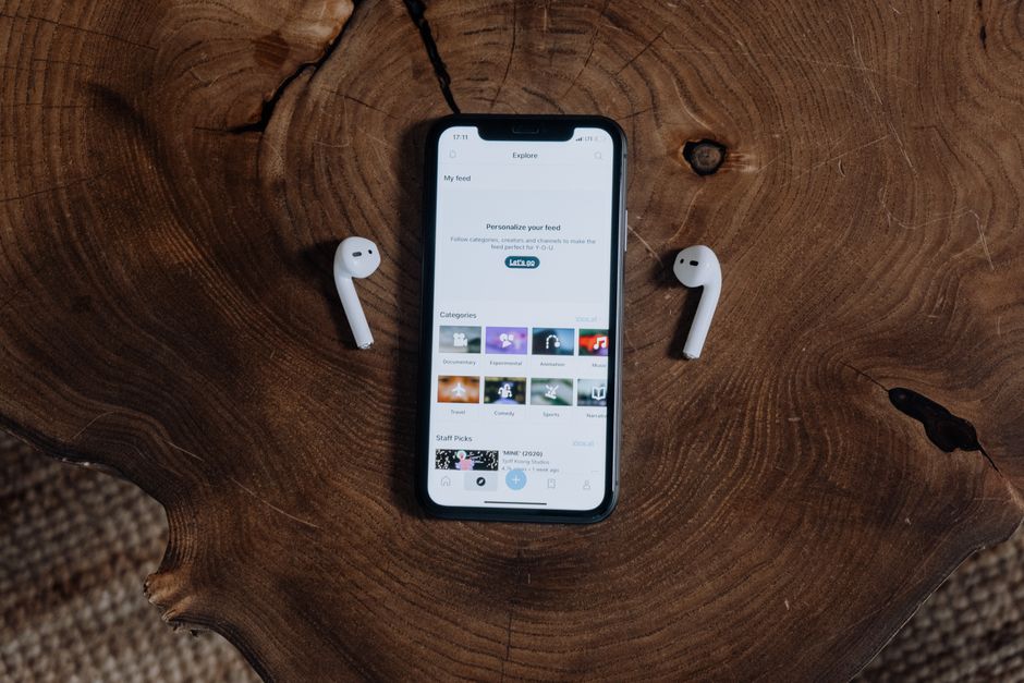 Un smartphone con auriculares inalámbricos sobre una superficie de madera rústica, mostrando tecnología moderna y estilo de vida.