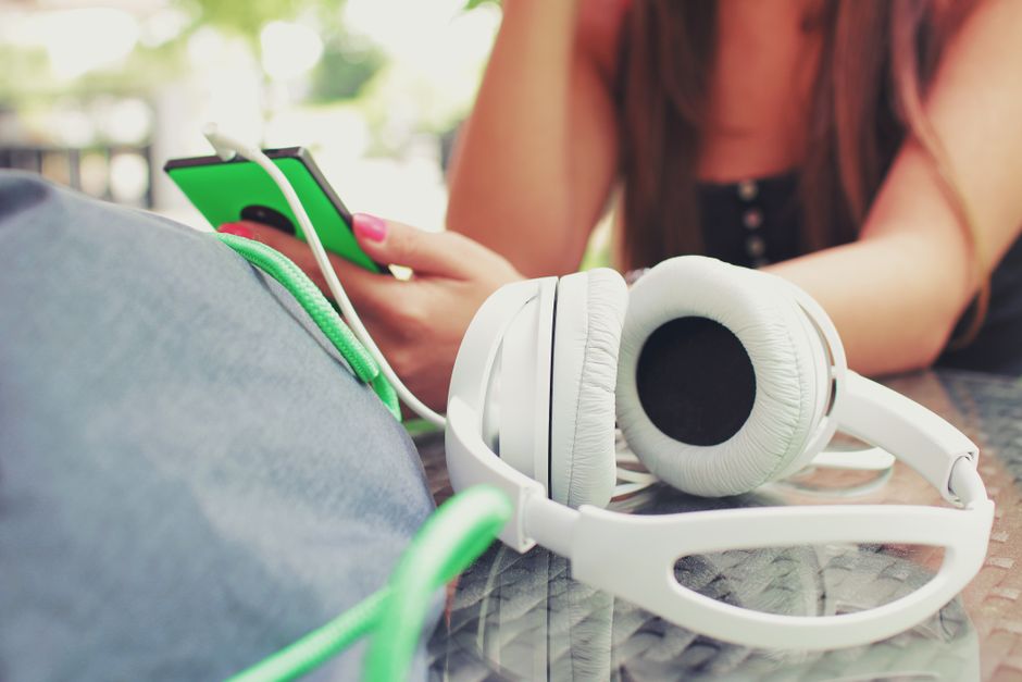 Una mujer escucha música con auriculares, utilizando un smartphone en un café al aire libre.
