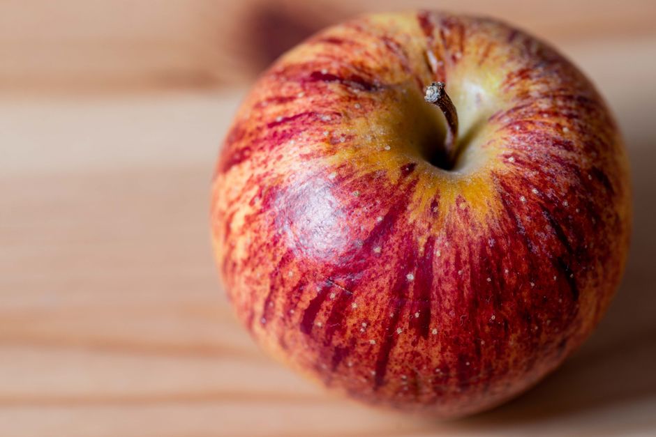 Primer plano vibrante de una manzana roja y amarilla sobre superficie de madera.