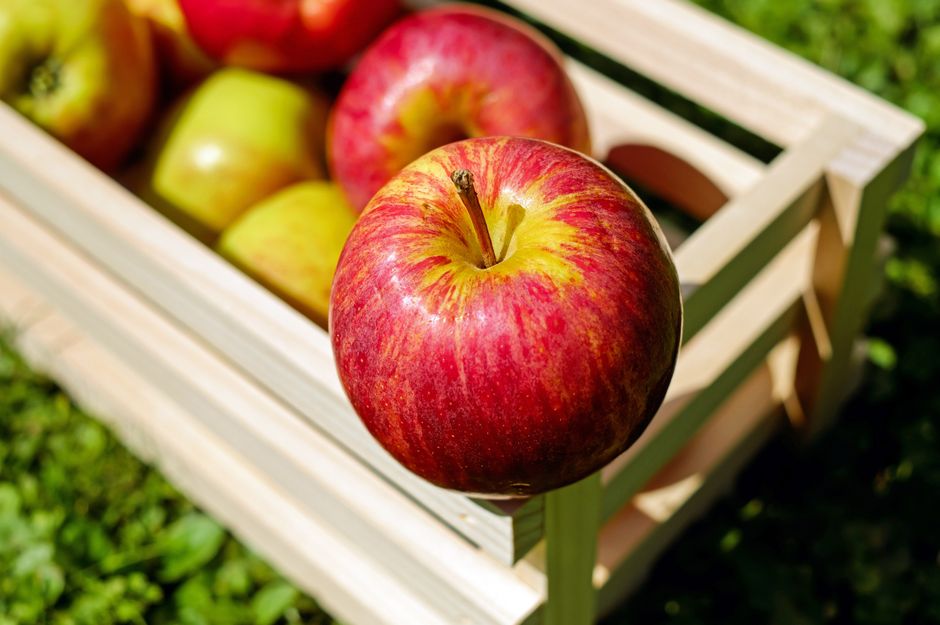 Manzanas rojas maduras en una caja de madera sobre la hierba, mostrando frutas frescas al aire libre.