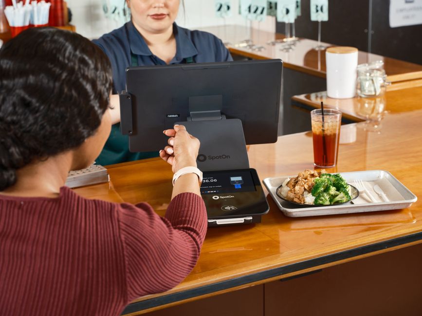 Un cliente utiliza su reloj inteligente para realizar un pago sin contacto en un restaurante con sistema de punto de venta SpotOn.
