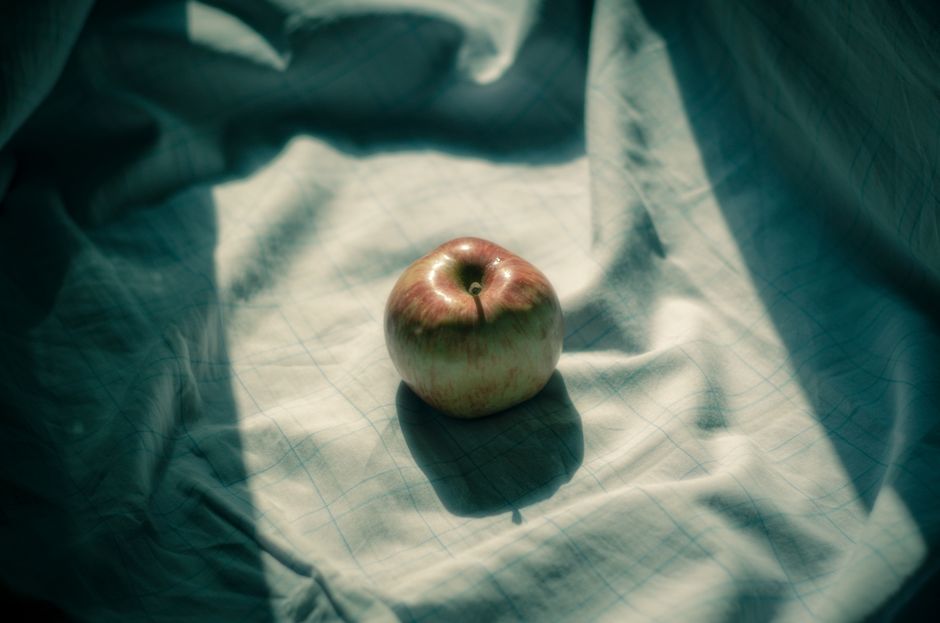 Una sola manzana se encuentra sobre un tejido doblado con luz suave y difusa creando sombras serenas.