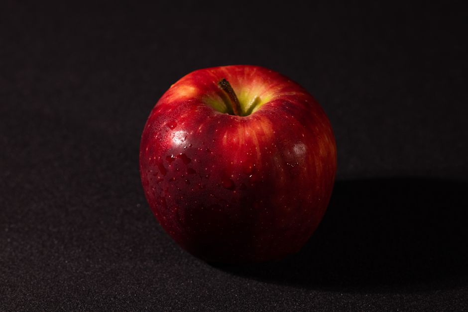 Una manzana roja fresca y brillante con gotas de agua contra un fondo oscuro, simbolizando salud.