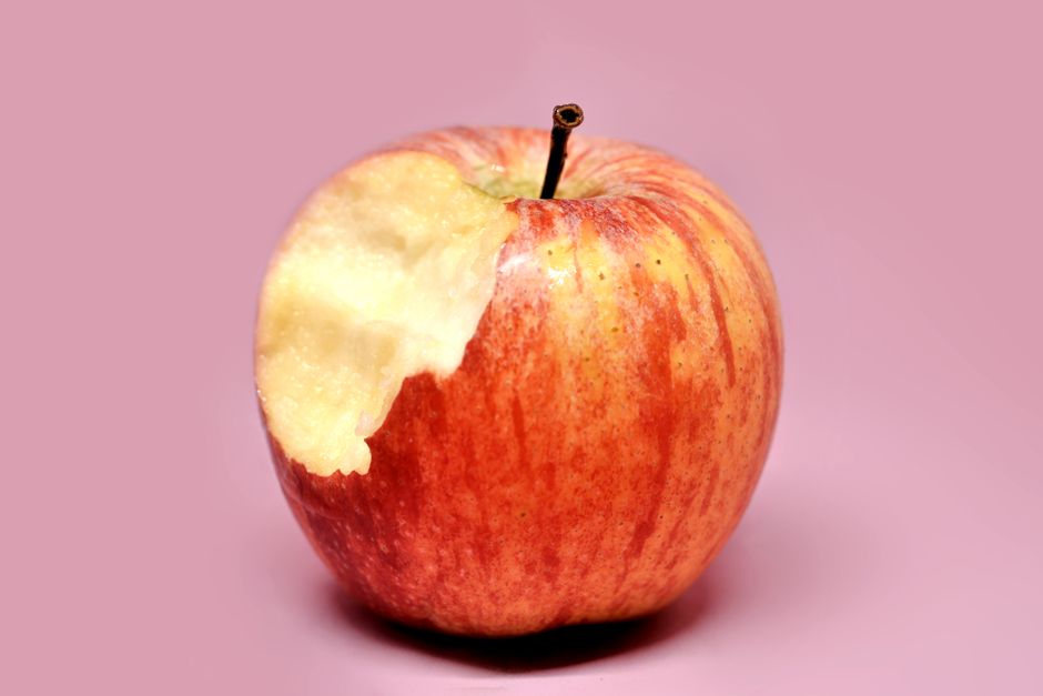 Primer plano de una manzana roja mordida, aislada sobre un fondo rosa.
