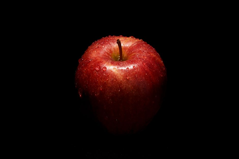 Primer plano de una vibrante manzana roja con gotas de agua sobre un fondo negro.